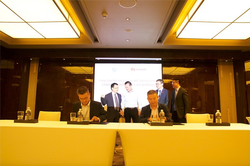 Huawei and Guizhou Yilong executives sitting at a desk at HUAWEI CONNECT 2018, signing an agreement on cloud data centers