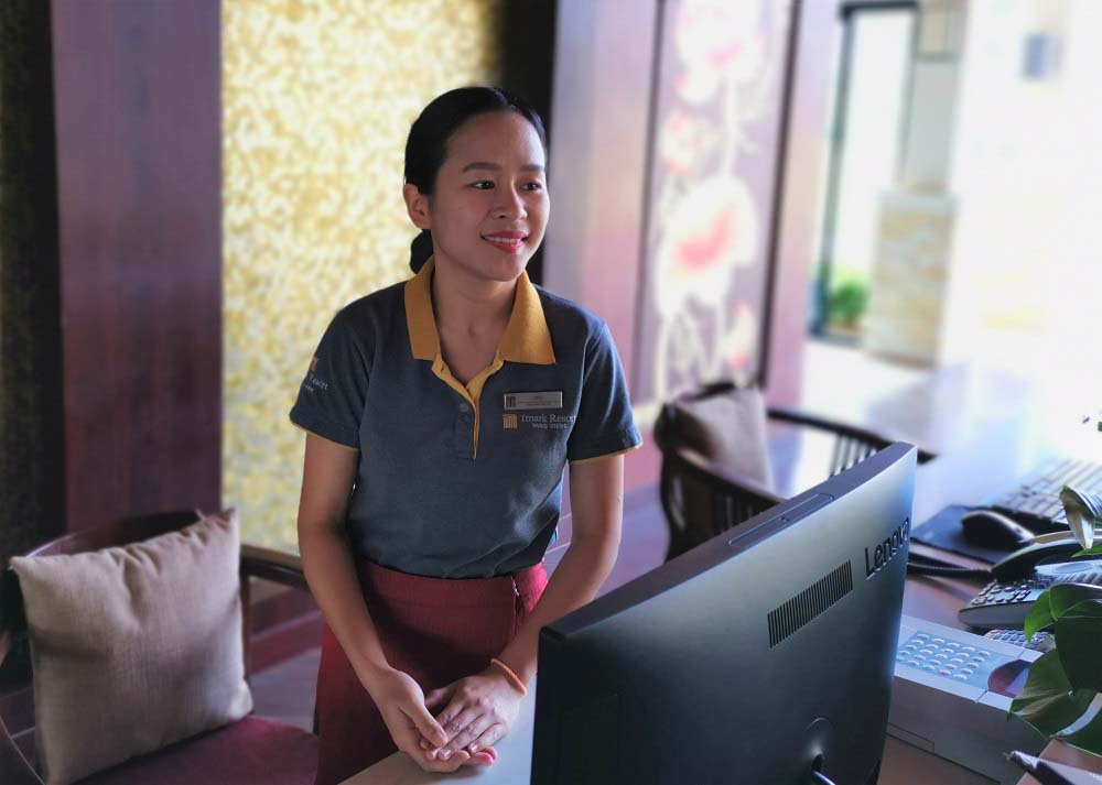 A portrait of Phokham, staff member of Tmark Resort Vangvieng, standing behind the customer desk of the hotel